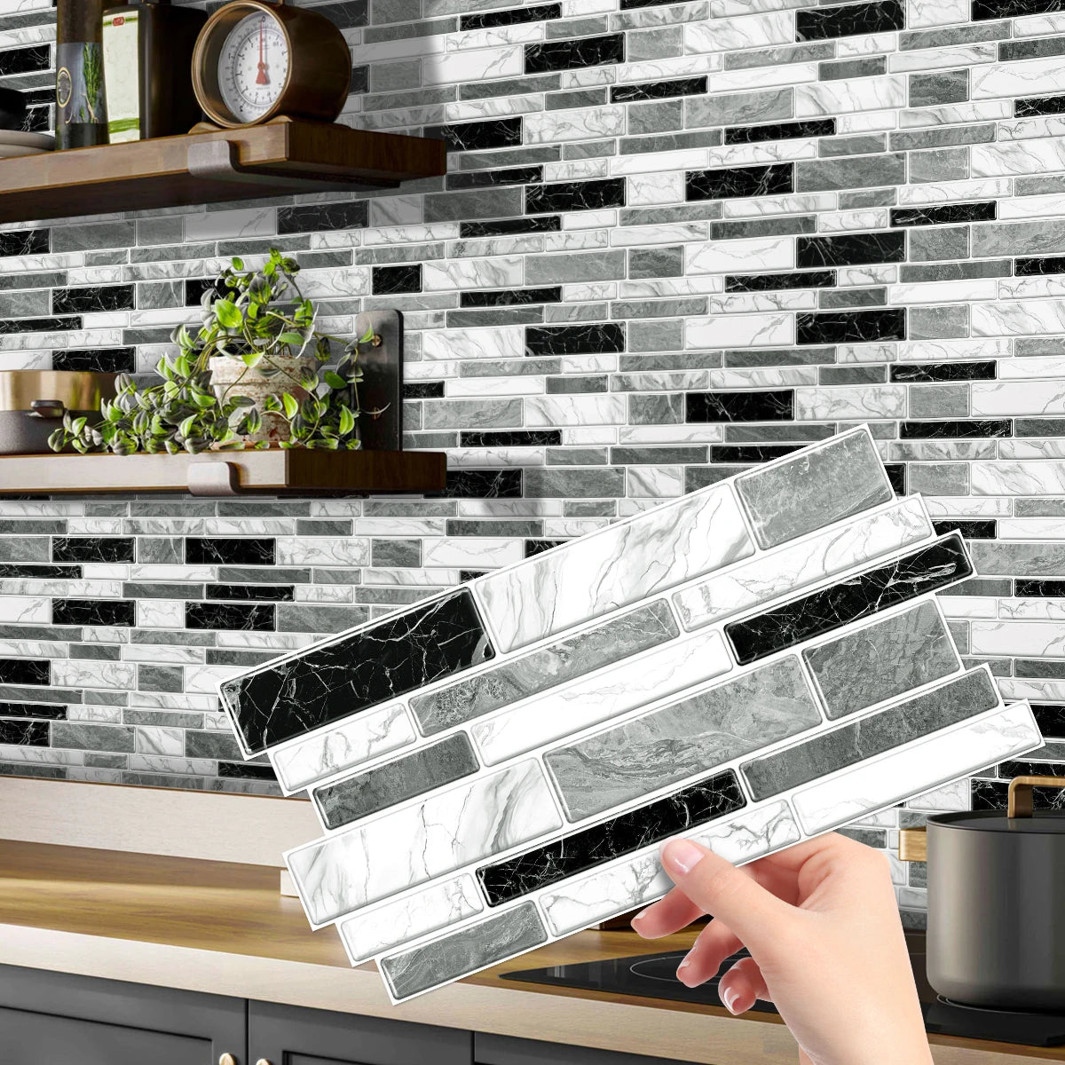 A hand is holding a stack of rectangular marble-patterned tile stickers against a black and white subway tile backsplash.