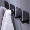 A set of four black adhesive stainless steel robe hooks mounted on a gray wall.