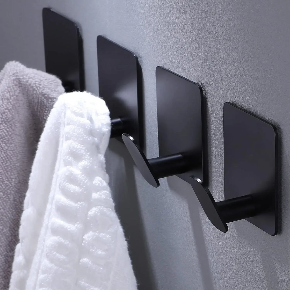 A set of four black adhesive stainless steel robe hooks mounted on a gray wall.