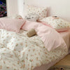 Pink floral bedding set featuring a duvet cover and pillows with white background and small pink flowers.
