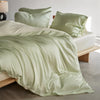 A light sage green luxury mulberry silk duvet cover set draped on a bed with matching pillows.