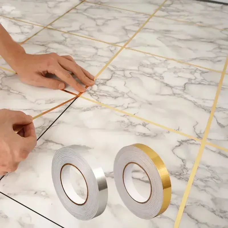 Hands are applying self-adhesive waterproof tile gap sealing tape along the grout lines of a marble floor.