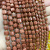 A hand holds a strand of reddish-brown natural stone square faceted beads for jewelry making.