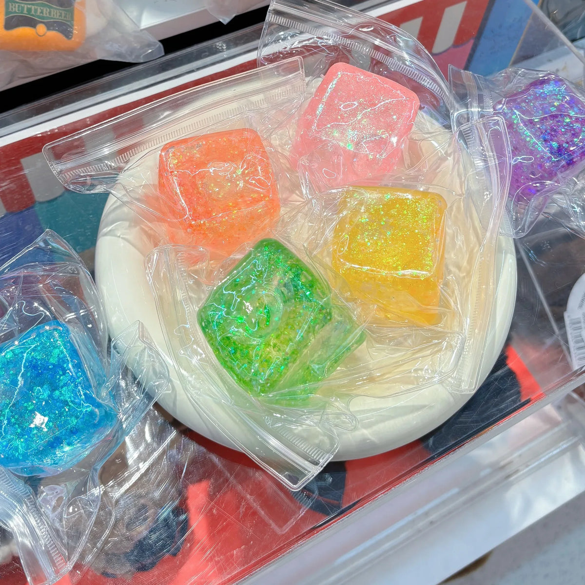 Ein durchsichtbarer Plastikbehälter mit mehreren farbigen quadratischen Stressball-Spielzeugen.