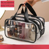 A clear PVC travel toiletry bag with black straps and medium double pockets is shown being held by a hand.