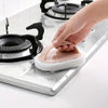 A hand is using a pink magic sponge scrubber with a long handle to clean a stovetop.
