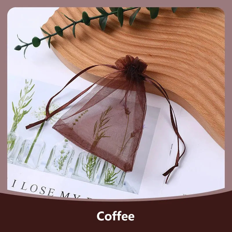 A dark brown organza drawstring gift bag with dried greenery is displayed on a wooden surface.