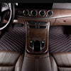 Interior view of a car showing brown leather seats and floor mats with red stitching and wood trim.