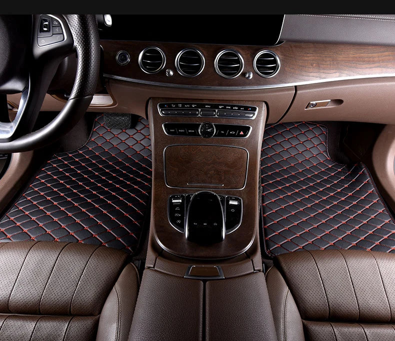 Interior view of a car showing brown leather seats and floor mats with red stitching and wood trim.