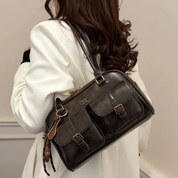 A woman holds a dark brown multi-pocket shoulder handbag with gold hardware against a light background.