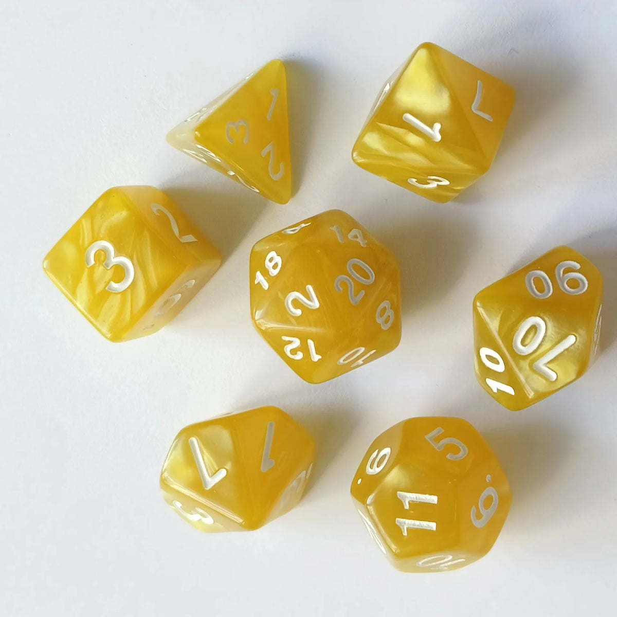 A collection of seven yellow translucent polyhedral dice arranged on a white surface.
