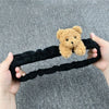 A hand holds a black plush bear and pig car rearview mirror cover.