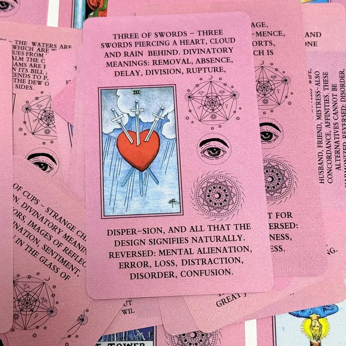 A pink Rider-Waite Tarot card depicting three swords piercing a heart with associated meanings.