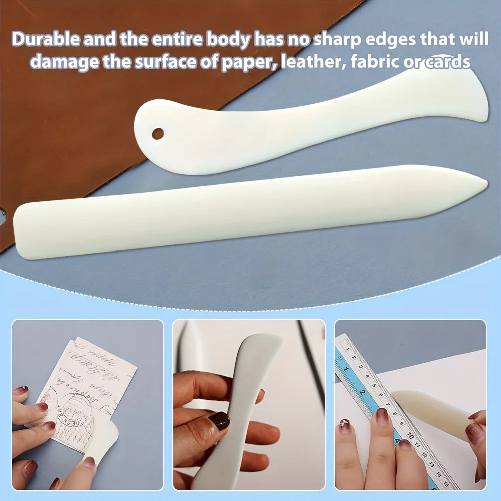 A white plastic bone folder and crease marker set shown with various craft materials like paper and leather.