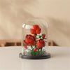 A clear glass dome display featuring a miniature red rose bouquet built from green and white building blocks.