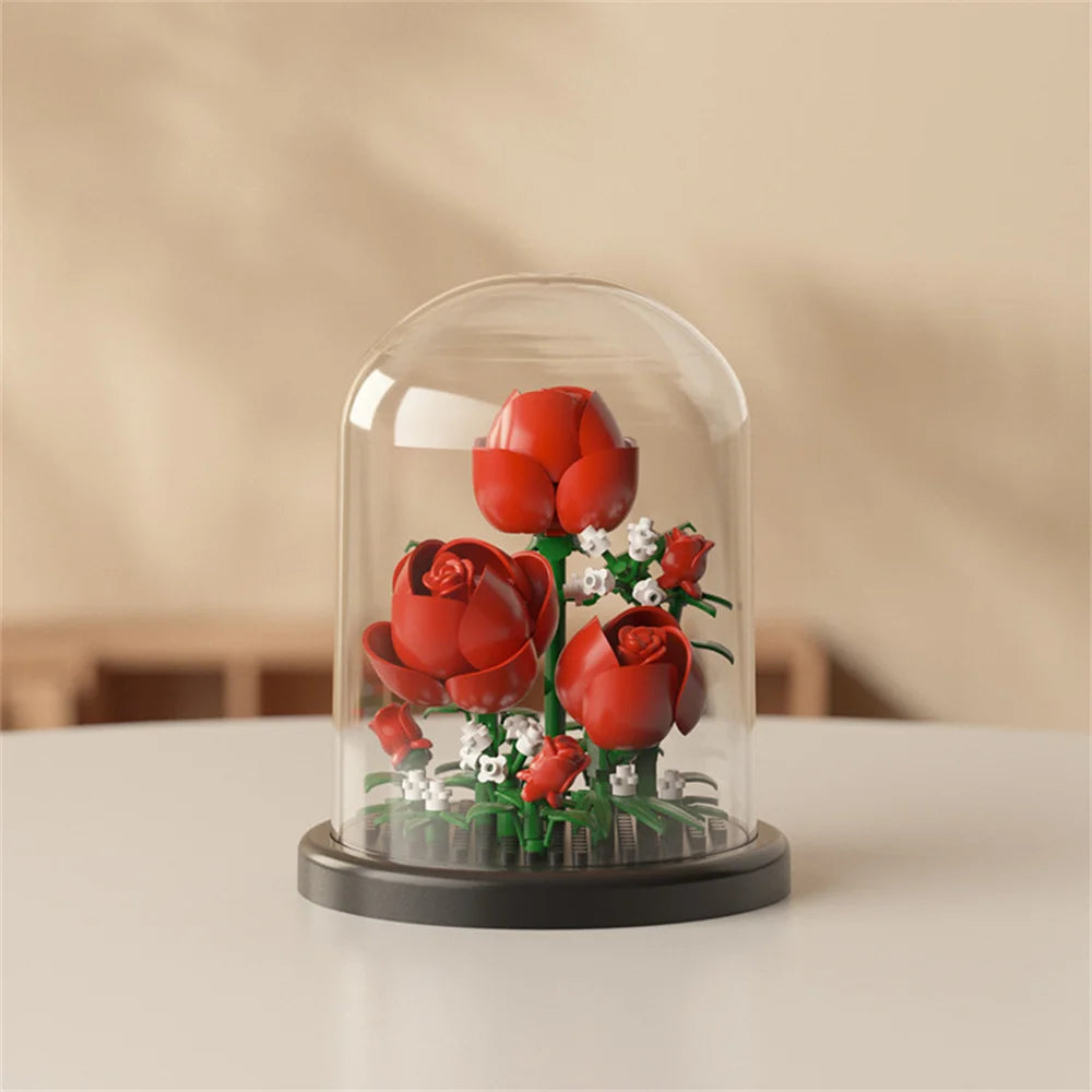 A clear glass dome display featuring a miniature red rose bouquet built from green and white building blocks.
