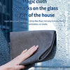 A hand is wiping a window with a gray microfiber cloth, demonstrating its ability to clean glass without leaving marks.