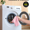 A hand places a pink reusable microfiber cleaning cloth into the drum of a white washing machine.