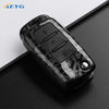 Black carbon fiber car key cover with electronic buttons resting on a dark surface.