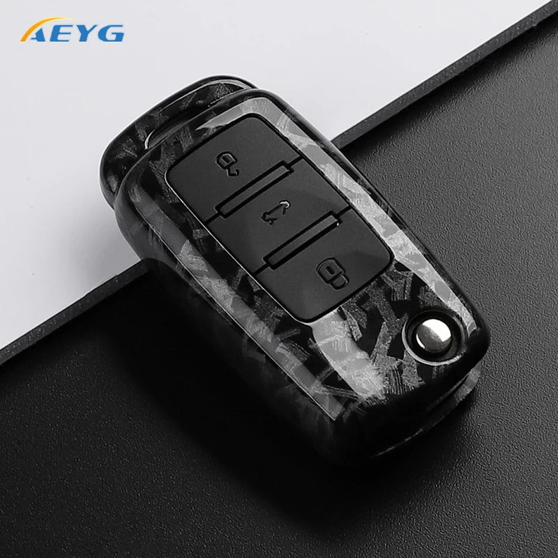 Black carbon fiber car key cover with electronic buttons resting on a dark surface.