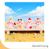 Four pink resin pig figurines with yellow and red accents displayed on a wooden surface amidst yellow sand.
