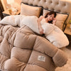 A woman relaxing under a large, fluffy beige and cream double-sided velvet quilt blanket in a bedroom setting.