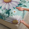 A hand is touching a fitted sheet featuring a white and purple daisy floral print on a teal background.