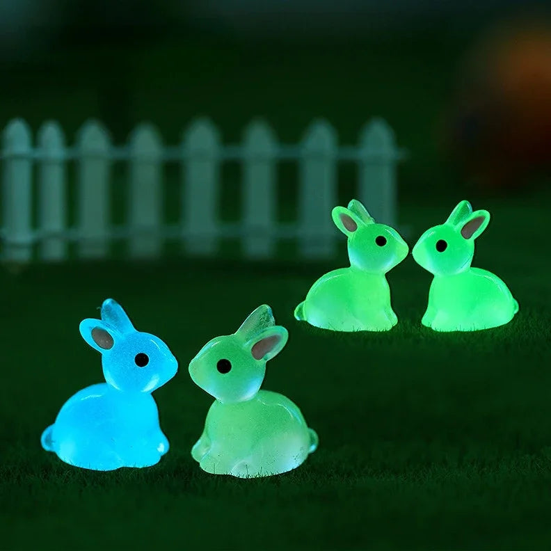 A set of three glowing green and blue resin miniature bunny figurines resting on a dark green surface.