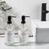 A set of two clear glass soap dispensers with black pumps for dish soap and hand soap on a white countertop.