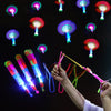 A hand launches an LED glowing flying arrow toy with a rubber band launcher, surrounded by various colored light effects.