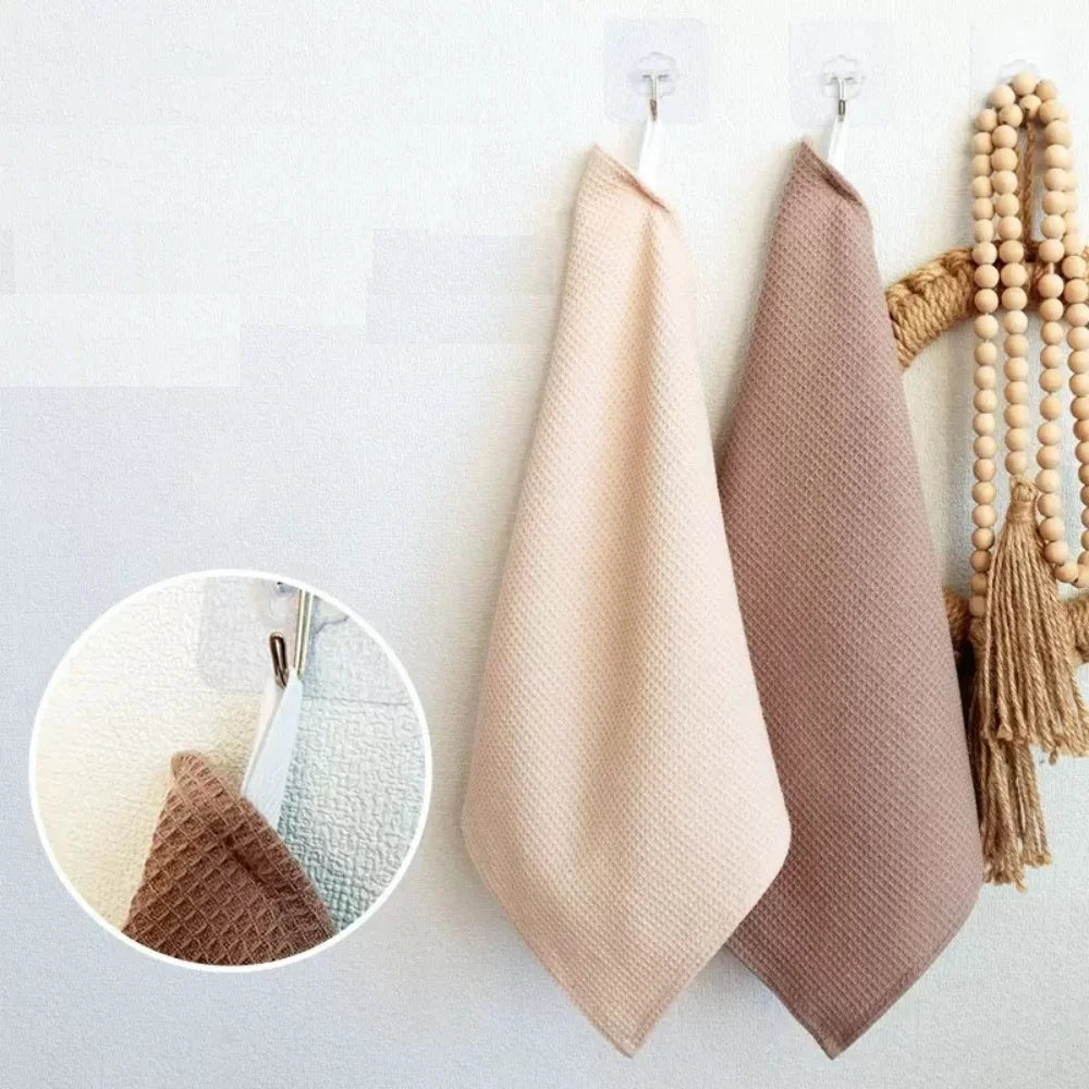 A set of four waffle weave towels in beige and taupe colors hanging on a white wall.