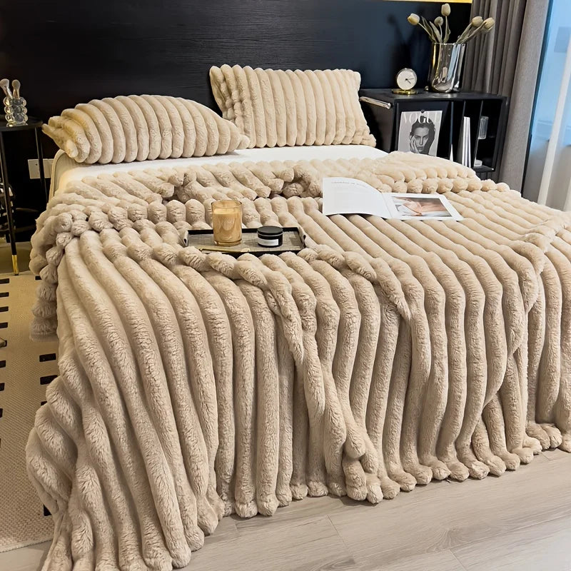 A thick, beige flannel blanket draped over a bed, featuring vertical pleats and a gold candle.