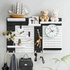 A black and white wall-mounted pegboard organizer with various hooks, storage boxes, and decorative items.