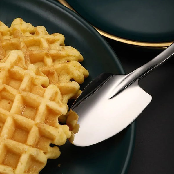 Une cuillère à glace en acier inoxydable argenté ramasse une waffle dorée d'une assiette vert foncé.