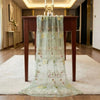 A sheer green tulle table runner with floral embroidery displayed on a dark wooden table.
