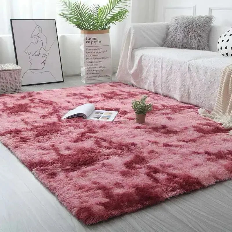 A plush, deep pink velvet carpet is displayed on a light floor, with a white bed and potted greenery in the background.