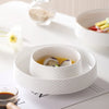 A white ceramic soup bowl filled with a light yellow broth and sliced mushrooms, set on a white plate.