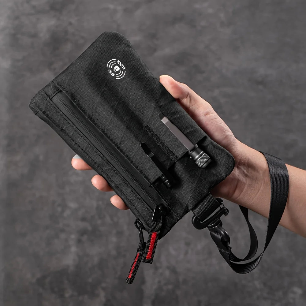 Une main tient un porte-monnaie clutch noir mince bloque RFID avec une sangle et un emplacement pour carte argenté.