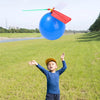 A young boy is throwing a blue propeller balloon helicopter toy into the air in a grassy field.