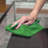 A hand is holding a bright green reusable microfiber cleaning towel roll on a glass surface.