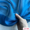 A hand is gently folding a piece of bright blue silk chiffon fabric.