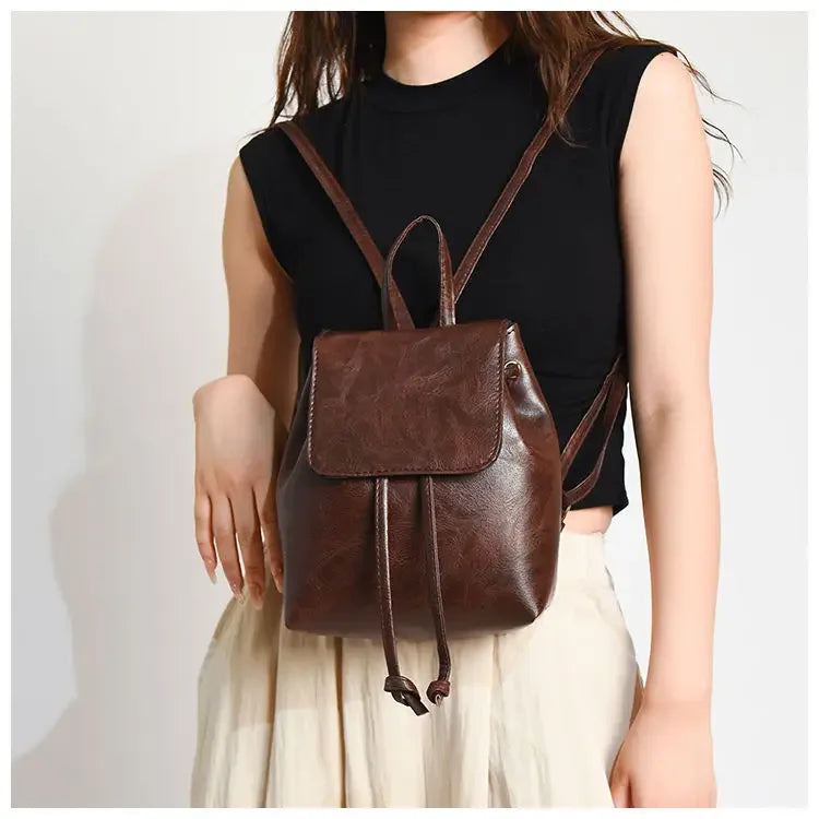 Une femme portant un haut noir et un pantalon clair, qui transporte un mini sac à dos de sport marron à cordon.