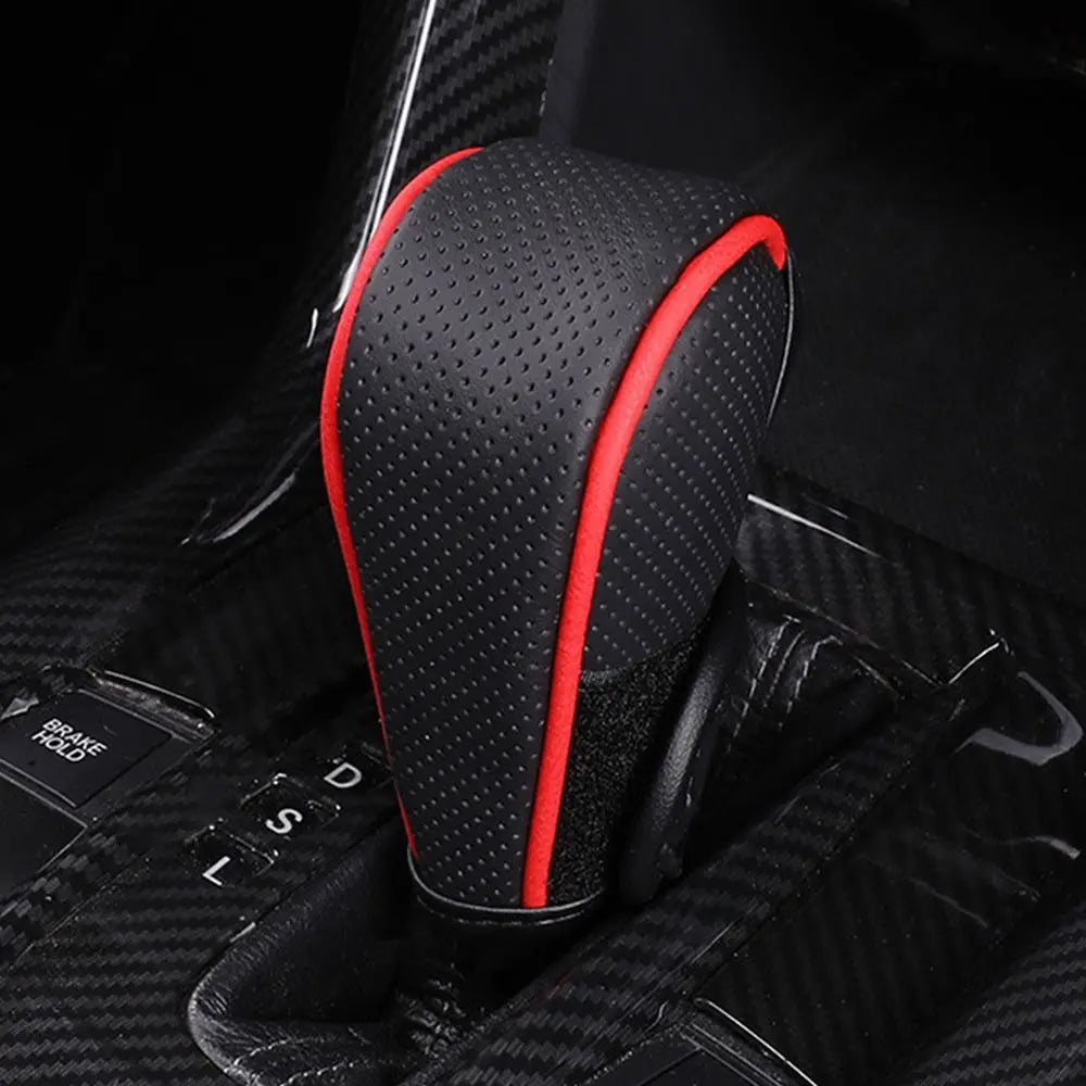 A close-up view of a black and red gear shift knob cover with a perforated texture resting on a black vehicle interior.