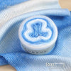 A roll of blue and white gradient cake yarn is displayed on a blue fabric background.