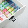A white storage box filled with silicone toilet lids and lifters in various pastel colors and patterns.