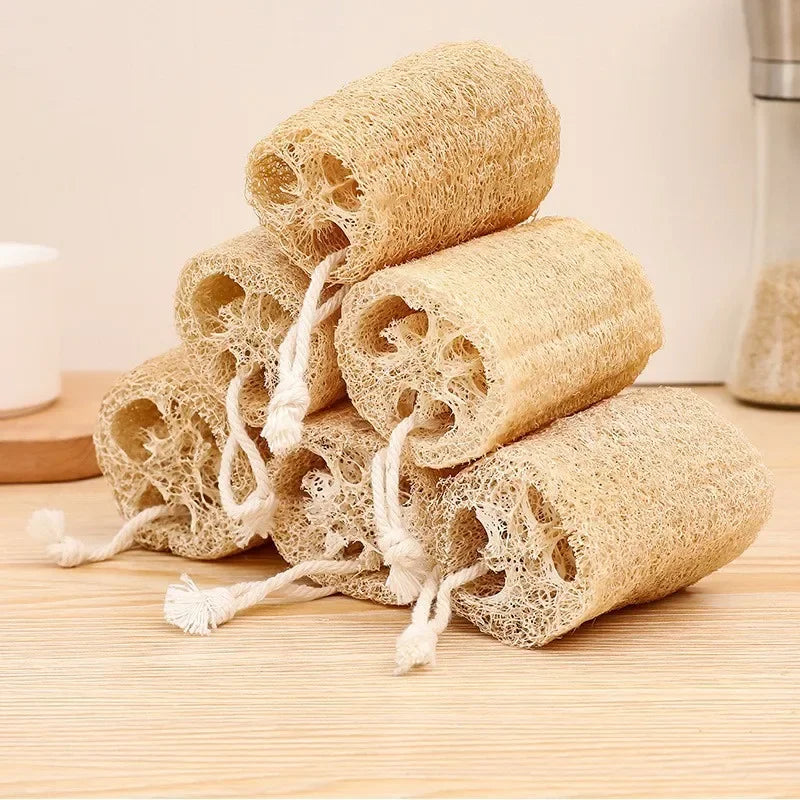 A stack of natural loofah body scrubbers with hanging ropes resting on a wooden surface.