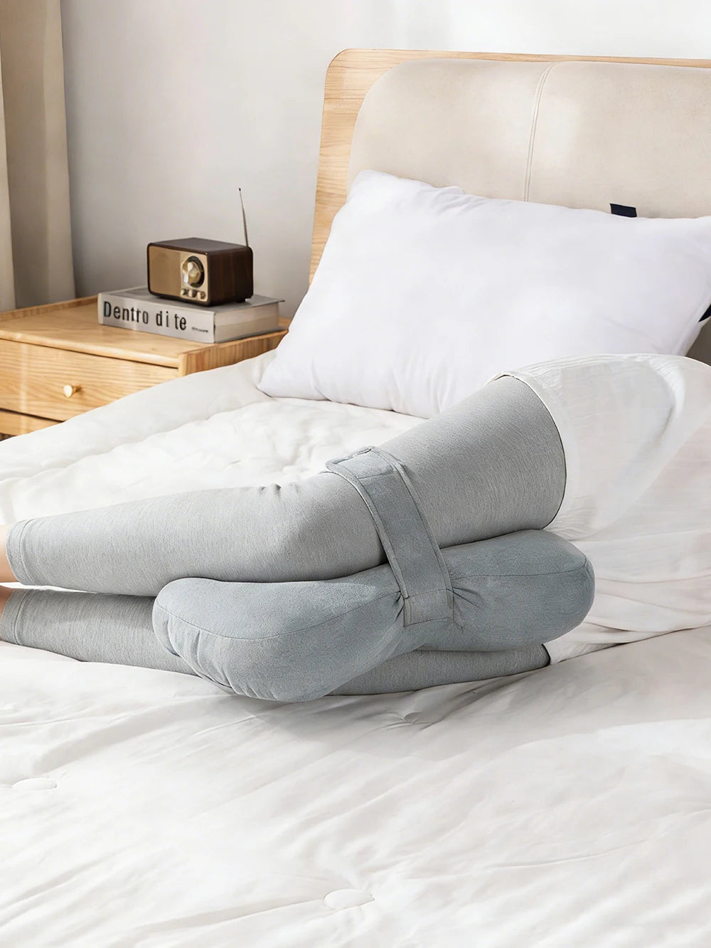Una almohada blanca y un par de almohadas de rodilla grises se exhiben en una cama con cabecero de madera.