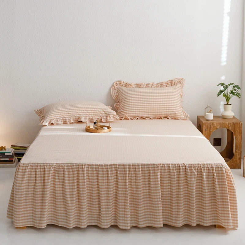 A beige plaid cotton bed skirt with a gathered hem and matching pillows on a light-colored bed.