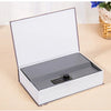A silver hidden book safe with a combination lock is shown open on a light wooden surface.