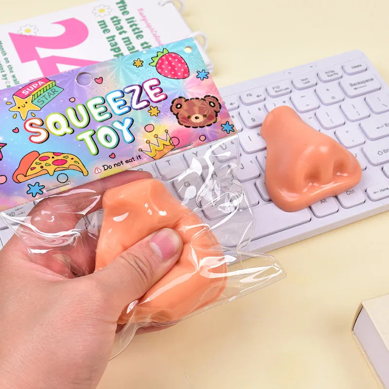 A hand holds an orange squishy pimple popper fidget toy next to a keyboard and a colorful toy package.